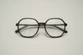 A pair of thick black-rimmed eyeglasses with clear lenses, resting on a textured gray carpet.