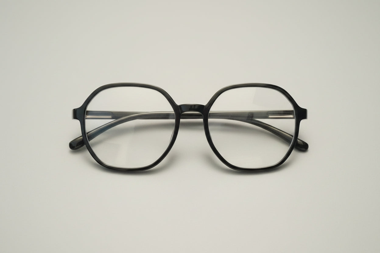 A pair of thick black-rimmed eyeglasses with clear lenses, resting on a textured gray carpet.