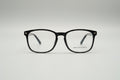 A pair of square-frame eyeglasses with a glossy black acetate frame and clear lenses, resting on a textured gray carpet.