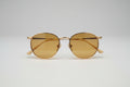 Round gold-framed eyeglasses with translucent lenses, resting on a dark textured carpet.
