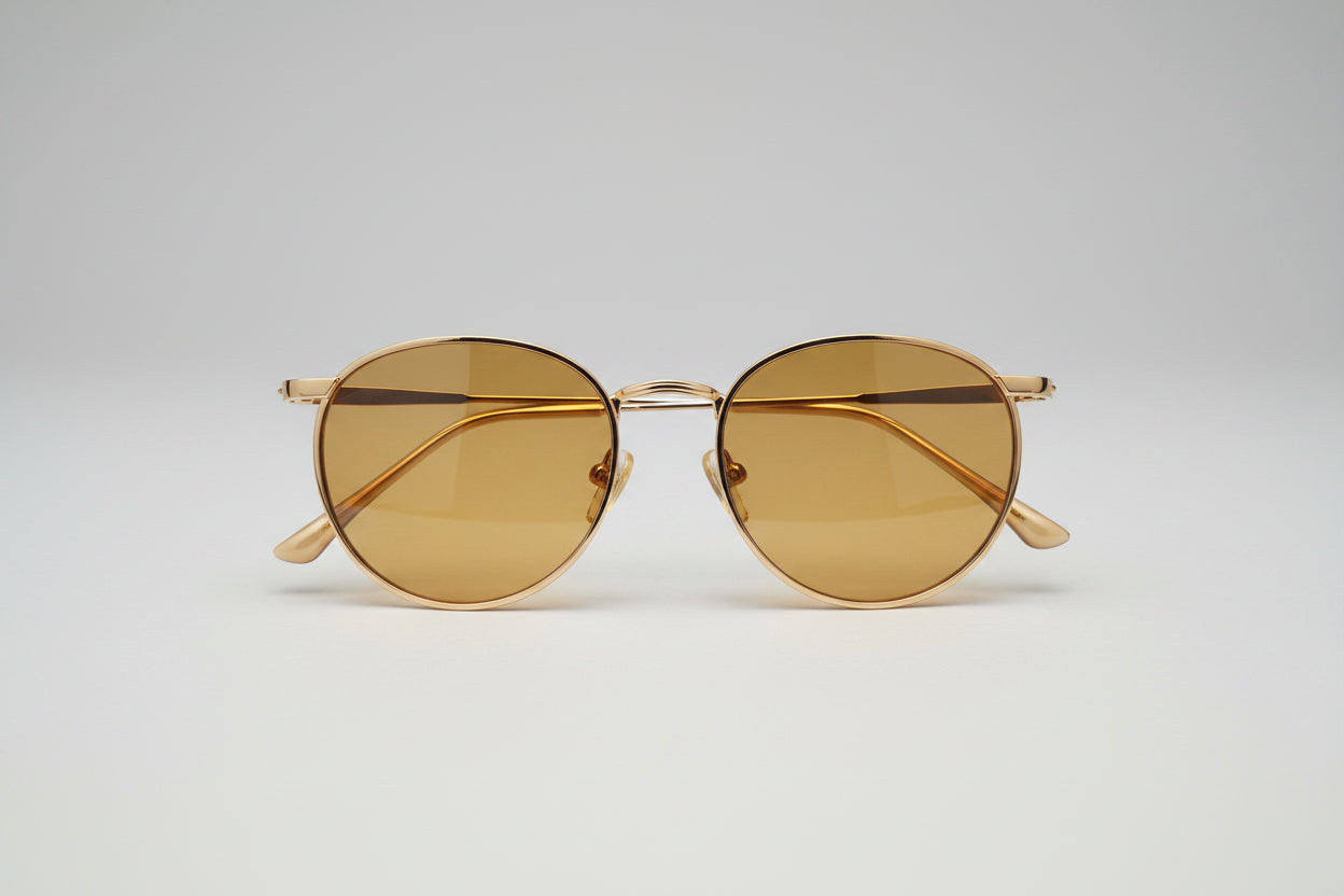 Round gold-framed eyeglasses with translucent lenses, resting on a dark textured carpet.